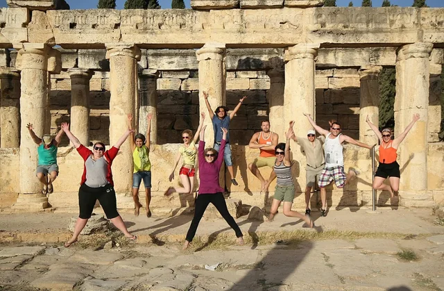 A tour group jumping together in front of ancient columns and carved stonework.