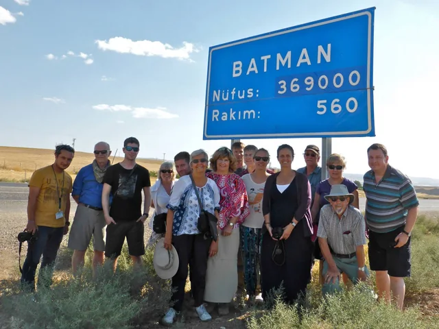 Travellers gathered beside a roadside sign for Batman during their journey.