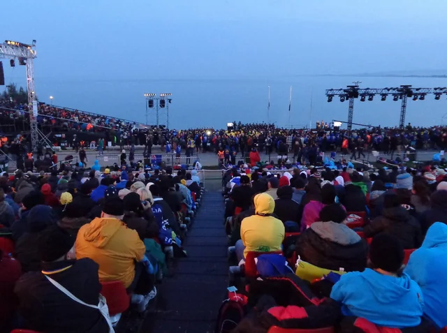 Visitors seated at an outdoor remembrance gathering beside the sea.