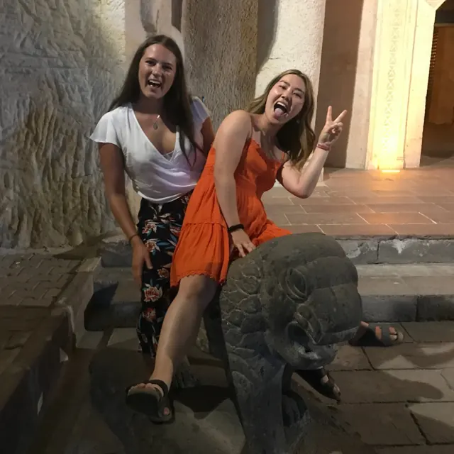 Two guests smiling beside a carved stone lion at night.
