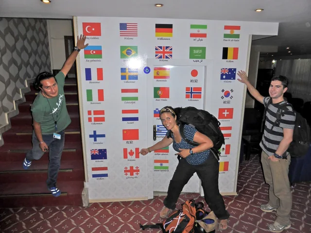 Three travellers beside a welcome display featuring flags and greetings from around the world.