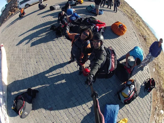 A traveller and pilot beside their paragliding equipment at a launch area.