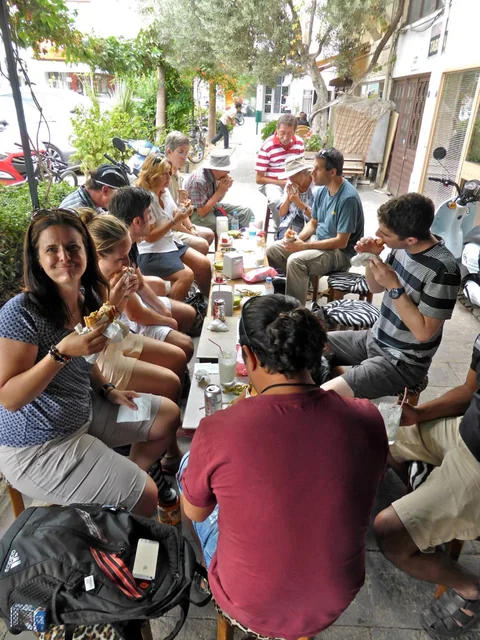 A tour group sharing a meal at an outdoor table on a village street.