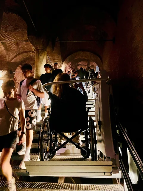 Visitors using a stair platform lift inside a historic vaulted passage.