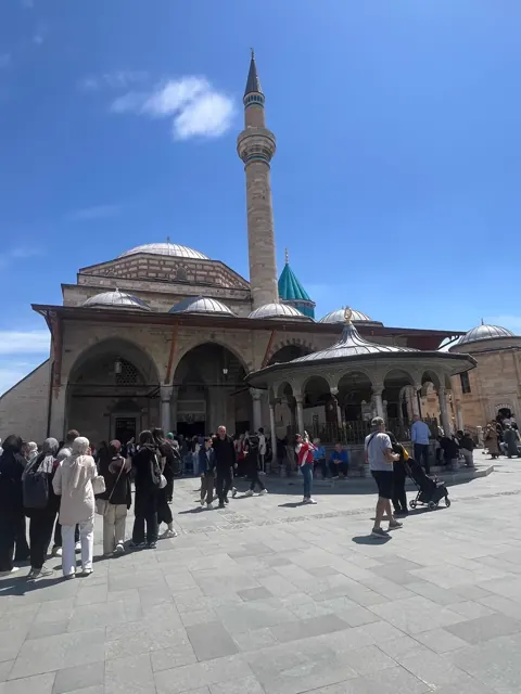 Visitors in the courtyard beside the turquoise dome of the Mevlana Museum, Konya.