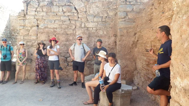 A guide speaking with a group beside ancient stone walls.