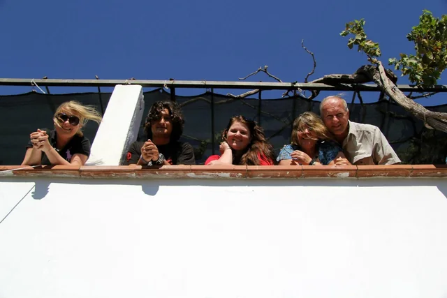 Five travellers leaning together over a terrace wall beneath a clear blue sky.