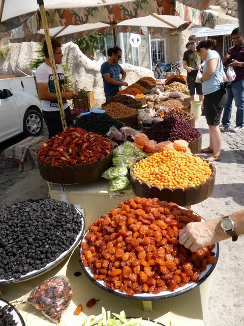 Shoppers browsing an outdoor market with baskets of olives and colourful produce.