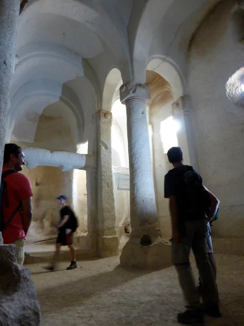 Visitors walking through a historic interior with pale stone columns and arches.