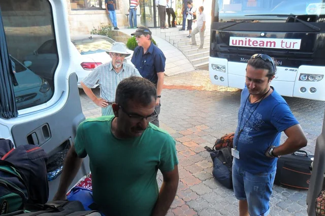 Travellers and their guide gathered beside luggage and tour vehicles.