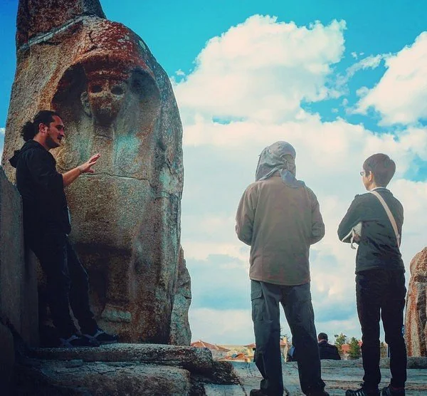 A guide speaking with travellers beside an ancient carved rock relief.