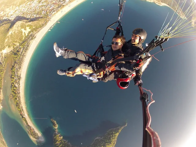 A traveller and pilot on a tandem paraglider above the coastline.