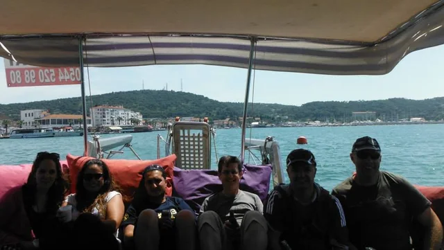 Travellers seated together beside the waterfront with boats and hills behind them.