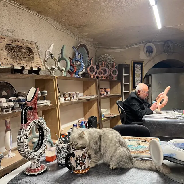 A cave pottery workshop A potter demonstrating ceramic work in a cave workshop, with a cat nearby.